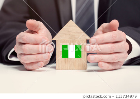 Businessman hand holding wooden home model with Nigerian flag. insurance and property concepts Businessman hand holding wooden home model with Nigerian flag. insurance and property concepts 113734979