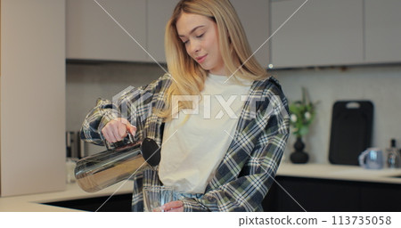 Woman pouring fresh water into glass from jug at home. Health and diet concept. Woman pouring fresh water into glass from jug at home. Health and diet concept. 113735058