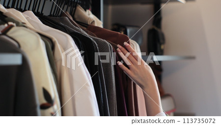 Close up woman choosing clothes from rack with hangers inside room. Lady looks to clothes, decides what to wear. Lifestyle women relax at home concept. Close up woman choosing clothes from rack with hangers inside room. Lady looks to clothes, decides what to wear. Lifestyle women relax at home concept. 113735072