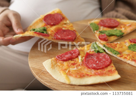 Pregnancy fast food. Close up view of young unrecognizable pregnant woman holding plate with tasty pizza enjoying unhealthy nutrition Pregnancy fast food. Close up view of young unrecognizable pregnant woman holding plate with tasty pizza enjoying unhealthy nutrition 113735081