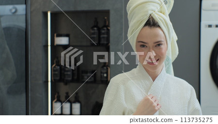 Portrait of young positive woman wearing bathrobe and towel on head after shower smiling to camera with mirror reflection. Natural make up, facial skincare. 113735275
