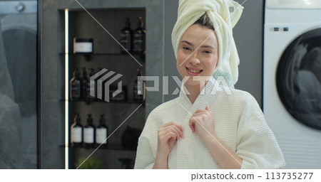 Portrait of young positive woman wearing bathrobe and towel on head after shower smiling to camera with mirror reflection. Natural make up, facial skincare. Portrait of young positive woman wearing bathrobe and towel on head after shower smiling to camera with mirror reflection. Natural make up, facial skincare. 113735277