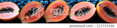Ripe papaya with blue companion fruits laid out on dark setting for healthy snacking 113735380