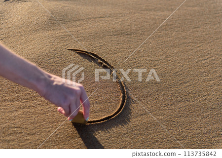 Young woman on the beach drawing a heart shape on the sand at sunset. Young woman on the beach drawing a heart shape on the sand at sunset. 113735842