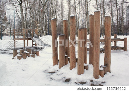 Wooden playground made of natural eco-friendly material in public city park with snow at winter time. Modern safety children outdoor equipment. Winter activities. Children rest and games on open air Wooden playground made of natural eco-friendly material in public city park with snow at winter time. Modern safety children outdoor equipment. Winter activities. Children rest and games on open air 113736622