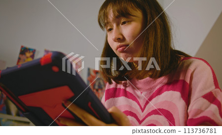 Teen girl chats or scrolls social networks using tablet computer in bedroom Teen girl chats or scrolls social networks using tablet computer in bedroom 113736781