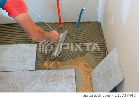 Preparing a concrete floor for tiling by troweling adhesive onto surface 113737448
