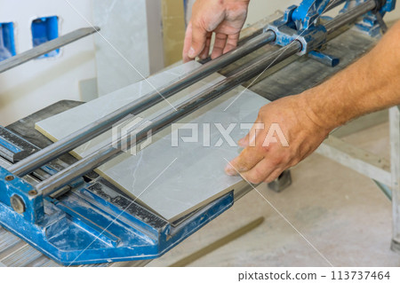Cutting ceramic tile with tile cutting hand machine is performed by a construction worker. 113737464