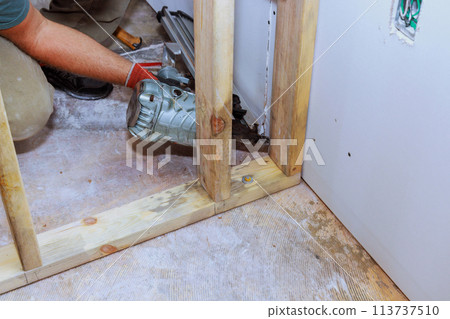Builder is using an air hammer to nail wooden beams to a housing frame 113737510
