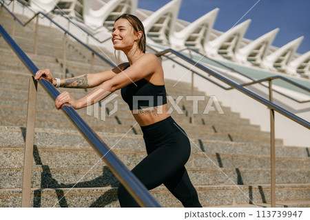 Smiling woman in sportswear have a rest after workout outside standing on building background Smiling woman in sportswear have a rest after workout outside standing on building background 113739947