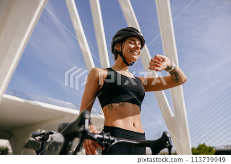 Female cyclist in helmet looking at smartwatch and counting calories burned. Healthy life concept  113739949