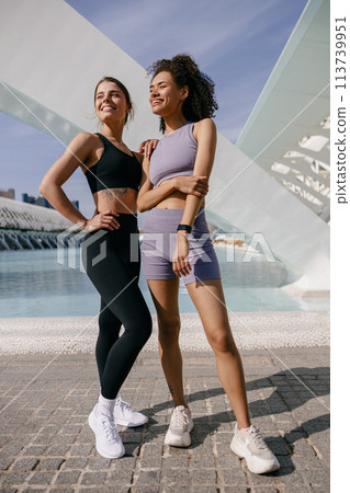 Smiling female sportswomen have a rest after morning jogging standing outdoors and looks away Smiling female sportswomen have a rest after morning jogging standing outdoors and looks away 113739951