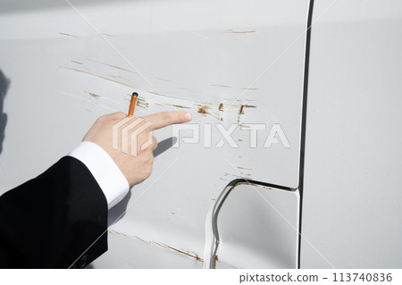 A worker's hand points to a scratch on a car 113740836