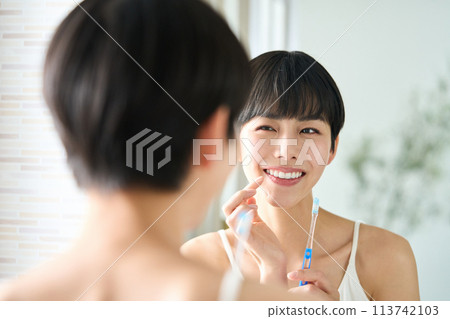 Woman brushing her teeth at the sink Woman brushing her teeth at the sink 113742103