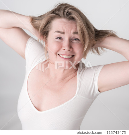 Portrait of mature adult woman with hands behind head and toothy smile. Happy woman is wearing bodysuit. High angle shot perfectly captures blonde woman's infectious energy and positive attitude 113743475