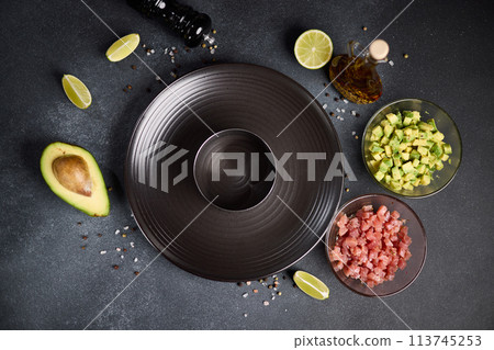 Tuna and avocado tartare recipe - sliced chopped ingredients and form on a dark table Tuna and avocado tartare recipe - sliced chopped ingredients and form on a dark table 113745253