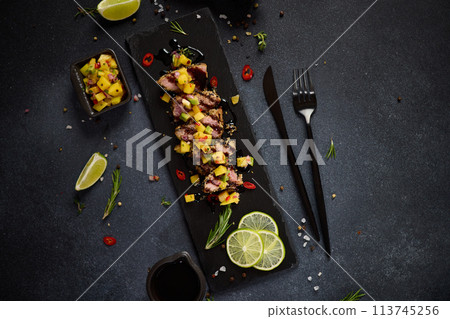 Sliced Organic grilled Tuna fillet covered with sesame seeds and mango salsa on black stone serving board Sliced Organic grilled Tuna fillet covered with sesame seeds and mango salsa on black stone serving board 113745256