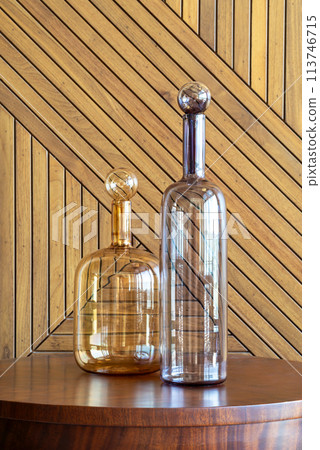 Two transparent glass decanters resting on a wooden surface, complemented by a herringbone-patterned wooden backdrop 113746715