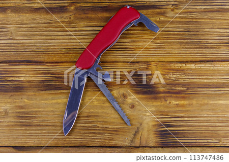 Red all purpose pocket knife on a rustic wooden background. Top view 113747486