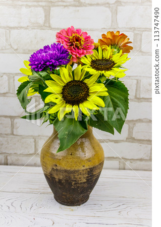 Bouquet of flowers in antique rustic clay jug against white brick wall Bouquet of flowers in antique rustic clay jug against white brick wall 113747490