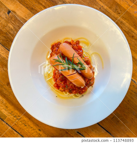 Hot dog or sausage stuffed with spaghetti in tomato pork sauce in white plate.Top view 113748893