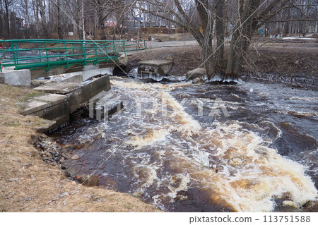 Spring flood. Rushing water in the river. Dark ferrous water rushes in the stream. Karelia, Lososinka River in spring. Floods, tsunami and climate change. Destroyed bridge with pipes. Weather disaster Spring flood. Rushing water in the river. Dark ferrous water rushes in the stream. Karelia, Lososinka River in spring. Floods, tsunami and climate change. Destroyed bridge with pipes. Weather disaster 113751588