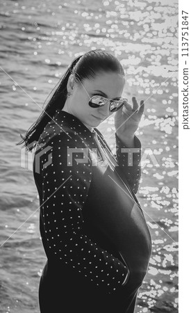 Black and white photo of a pregnant girl with glasses on the background of the sea 113751847