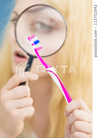 Woman looking at toothbrush through loupe 113752042