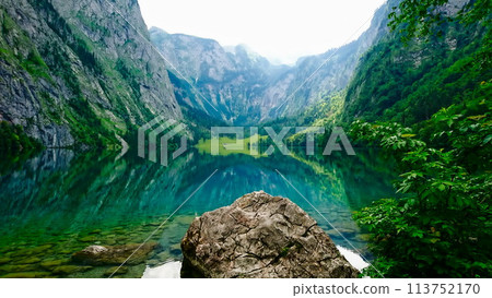 Konigssee, Germany - 06.16.2018: Obersee on a sunny day with peaceful water and forest on the side Konigssee, Germany - 06.16.2018: Obersee on a sunny day with peaceful water and forest on the side 113752170