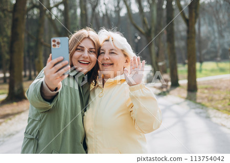 Happy older Mother and adult daughter are doing Selfie on city street. Outdoor shot of well-dressed female friends. Two women together doing selfie shot on mobile cell phone. Family day concept. Happy older Mother and adult daughter are doing Selfie on city street. Outdoor shot of well-dressed female friends. Two women together doing selfie shot on mobile cell phone. Family day concept. 113754042