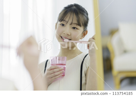 A primary school girl brushing her teeth with a smile while looking in the mirror in the morning 113754185