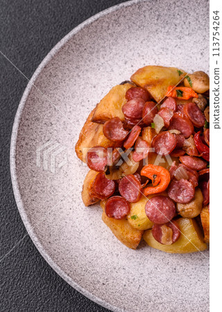 Grilled potatoes cut into slices with hunting sausages with garlic, onion 113754264