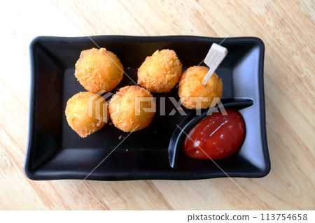 Fried cheese ball on black dish with tomato sauce. 113754658