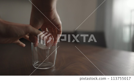 man put ice ball into tumbler gllass on walnut table 113755017