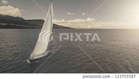 Sun reflection over yacht cruising at crystal sea bay aerial. Mesmerezing seascape with sail boat at summer bright sunlight day. Serene waterfront with alone sailboat at windy wheather at drone shot 113755597