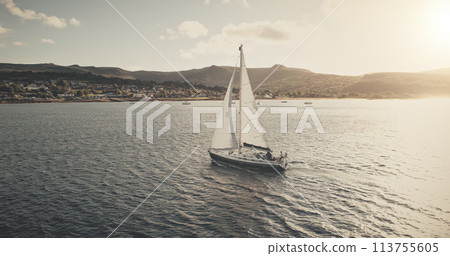 Sun seascape with white sailboat aerial. Mesmerezing landscape with sail boat at summer. Sunlight over sail boat at ocean bay. Sea shore of Arran Island with vessel. Serene water scenery drone shot Sun seascape with white sailboat aerial. Mesmerezing landscape with sail boat at summer. Sunlight over sail boat at ocean bay. Sea shore of Arran Island with vessel. Serene water scenery drone shot 113755605