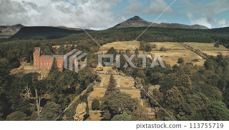 Scotland's ocean landscape shore aerial shot: trees and road with cars near Firth-of-Clyde Gulf. Magnificent coastline of nature with historical heritage: Brodick castle and wide shot 113755719