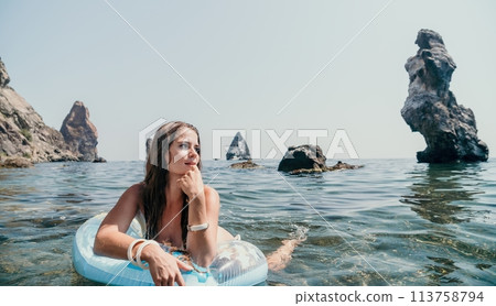 Woman summer sea. Happy woman swimming with inflatable donut on the beach in summer sunny day, surrounded by volcanic mountains. Summer vacation concept. Woman summer sea. Happy woman swimming with inflatable donut on the beach in summer sunny day, surrounded by volcanic mountains. Summer vacation concept. 113758794