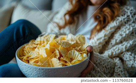Bowl potato chips by the television. Modern TV set indoors, focus on bowl of chips. Female eating snack and watching tv. Bowl potato chips by the television. Modern TV set indoors, focus on bowl of chips. Female eating snack and watching tv. 113760028