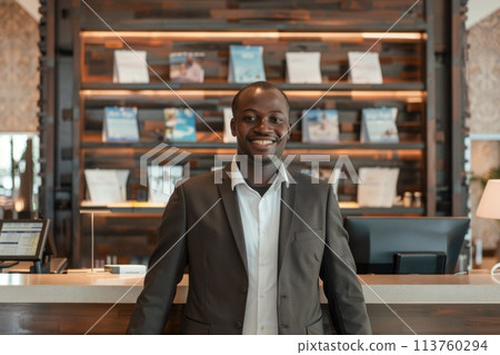 Smiling professional hotel concierge standing confidently at reception desk 113760294