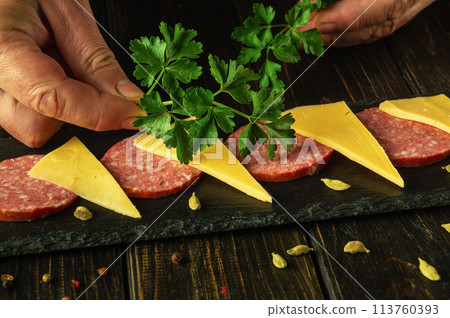 Close-up of a chef hands serving a cheese and sausage appetizer on a kitchen table before serving in a restaurant 113760393