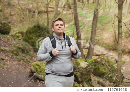 Young male with backpack hiking on the road in nature. 30s men in sport clothes walking on woodland. Guy portrait lifestyle. High quality photo. Wanderlust travel concept, atmospheric moment 113761638