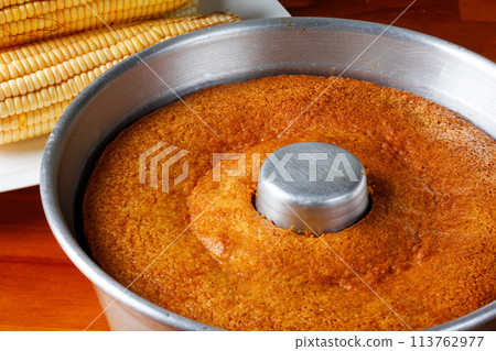 corn cake in the pan baking form on rustic wooden table. Typical Brazilian party food. Selective focus corn cake in the pan baking form on rustic wooden table. Typical Brazilian party food. Selective focus 113762977