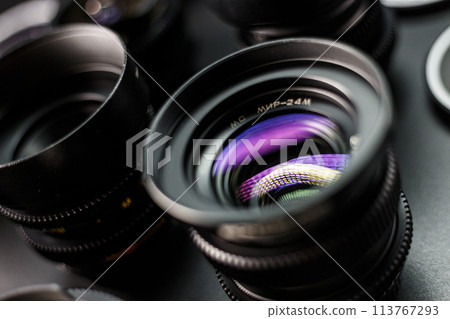 Vivid reflection on the glass of a vintage MC lens, detailed view of photographic collection, lenses in soft focus in the background 113767293