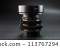 Vintage camera lenses stacked, 72mm marking on top, detail of aperture scale visible, essential for professional photography, set against a dark background. 113767294