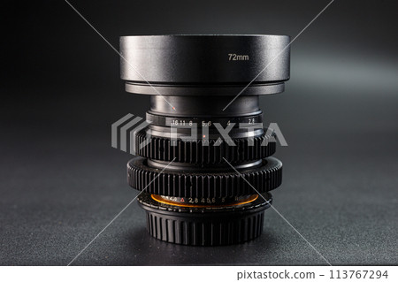 Vintage camera lenses stacked, 72mm marking on top, detail of aperture scale visible, essential for professional photography, set against a dark background. 113767294