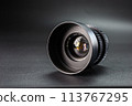 Slanted black camera lens capturing clear reflections, marked with 2.8 37 , premium photography equipment against a dark, soft-focus background 113767295