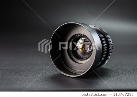 Slanted black camera lens capturing clear reflections, marked with 2.8 37 , premium photography equipment against a dark, soft-focus background Slanted black camera lens capturing clear reflections, marked with 2.8 37 , premium photography equipment against a dark, soft-focus background 113767295