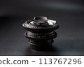 Stacked vintage camera lenses with a focus on the serial number, reflective glass surface, photography tools against a dark gradient background. 113767296