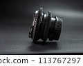 Side view of antique camera lens with distinct engravings and focus dials, part of a photography collection, against a moody dark background 113767297